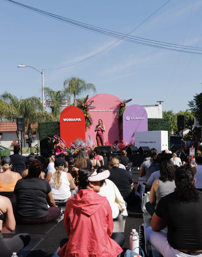 Outdoor stage on Whittier Blvd with Wellbeing en Comunidad arches, audience seated on the street